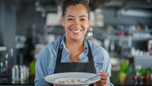 Cuisine de restaurant : Portrait d'une femme noire chef prépare un plat, goûte des aliments, en profite. Le cuisinier professionnel mange des plats délicieux, authentiques et traditionnels en utilisant uniquement des ingrédients sains pour la recette de repas